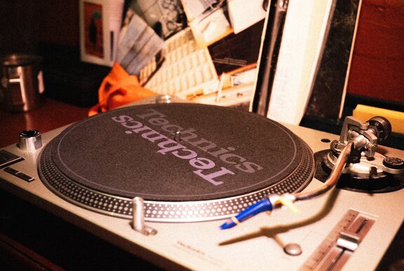 A turntable with a stack of vinyl records standing behind it.