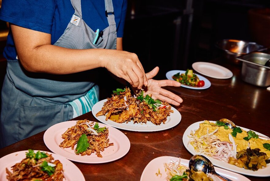 A chef plating up three Thai-style dishes with green garnishes.