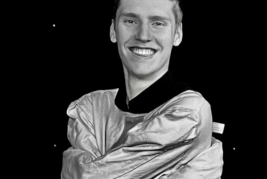 Magician and performer Mason Fewster smiling at the camera, wearing a straight jacket, his arms wrapped around his chest..