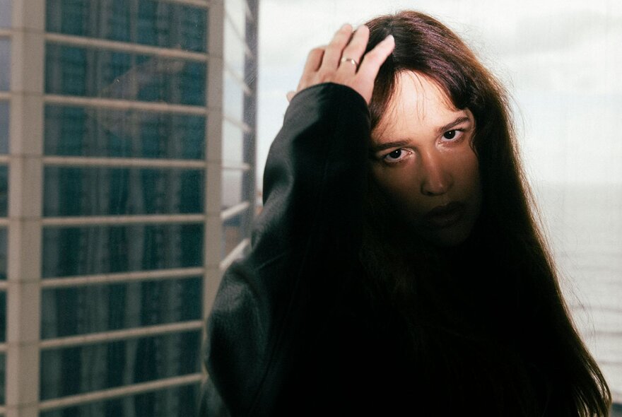 A person with their face partly obscured by shadows and their hand, which they are resting on the top of their head.
