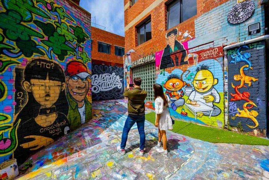 A couple standing in a colourful street art laneway taking photos