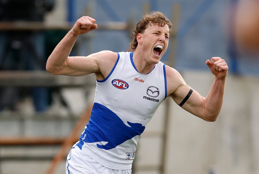 A North Melbourne AFL player celebrating on the field with his fists clenched above his head.