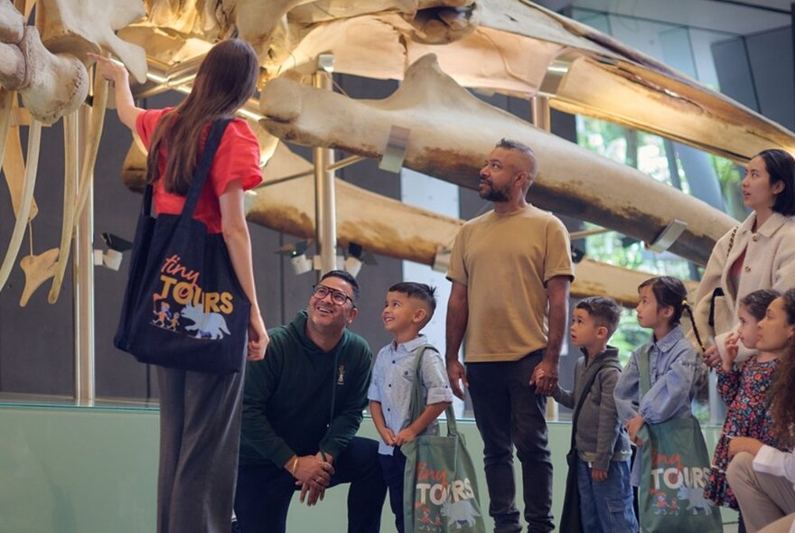 A family group on a guided tour through the Melbourne Museum, looking at a blue whale skeleton.