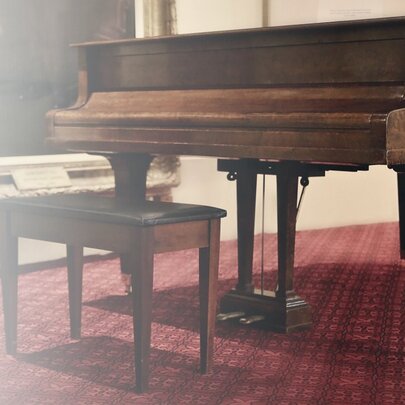A flared photo showing a grand piano and matching piano stool, in a red carpeted room with cream coloured walls. 