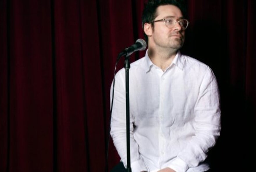 Man wearing white shirt, seated in front of a microphone.