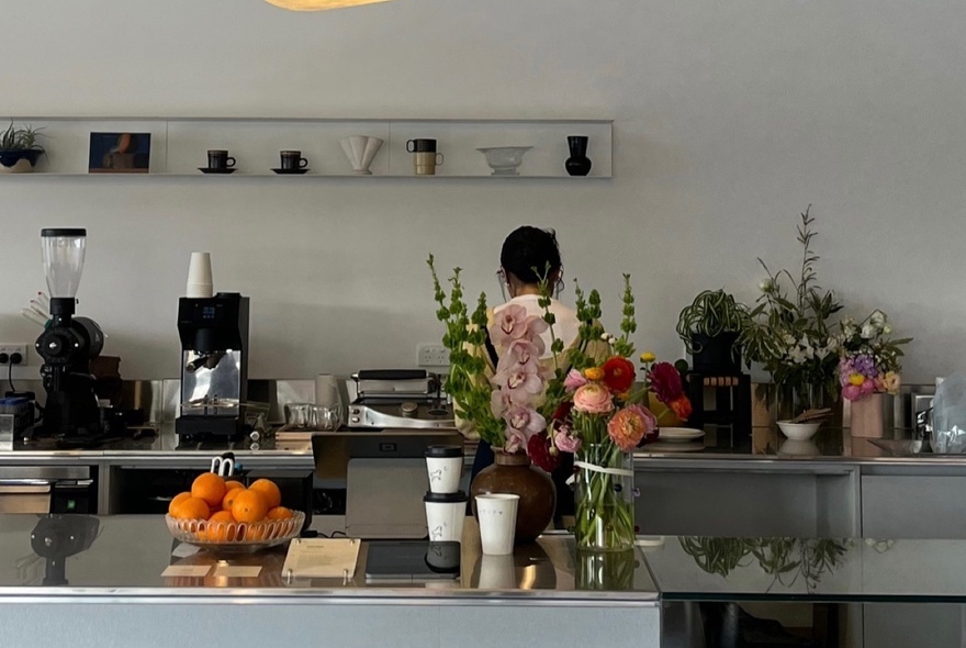 A cafe counter with coffee making equipment on display and a bowl of oranges.