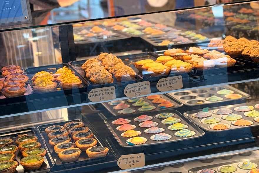 The glass display counter in a bakery with trays of flaky small tarts and rainbow coloured pastries for sale.