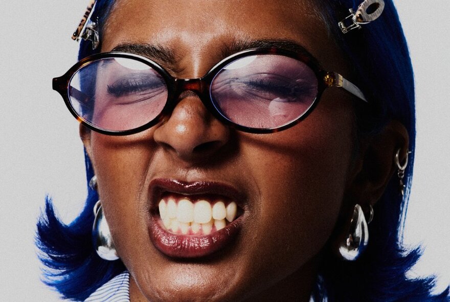 Singer Charlotte Dirckze posing for the camera, wearing glasses, her eyes closed and her teeth bared.  