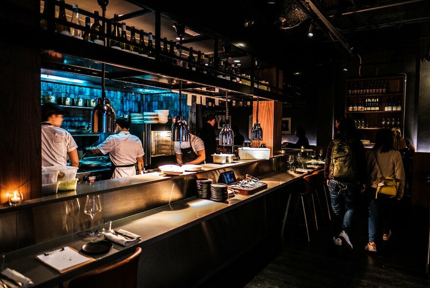 A dark restaurant with chefs at work in the open kitchen. 