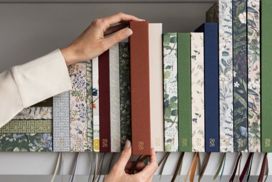 Some taking a journal from a shelf of colourful and floral journals.