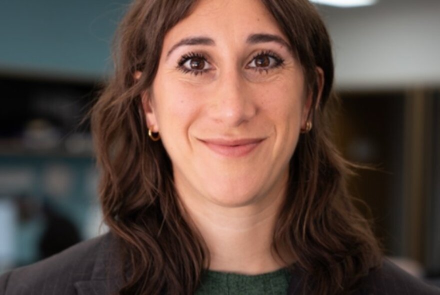 Sarah Schwartz, a woman with brown wavy hair, smiling and looking straight at the viewer. 