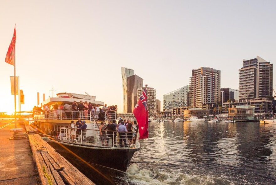 A small cruise ship with patrons on board about to take off on the Yarra River at sunset. 