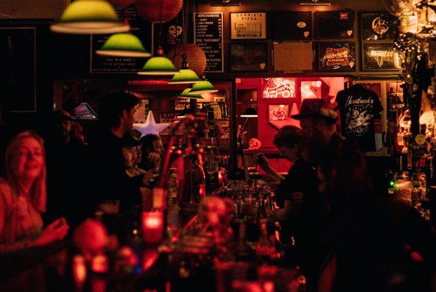 A dimly-lit bar with a red glow and green drop down lights. 