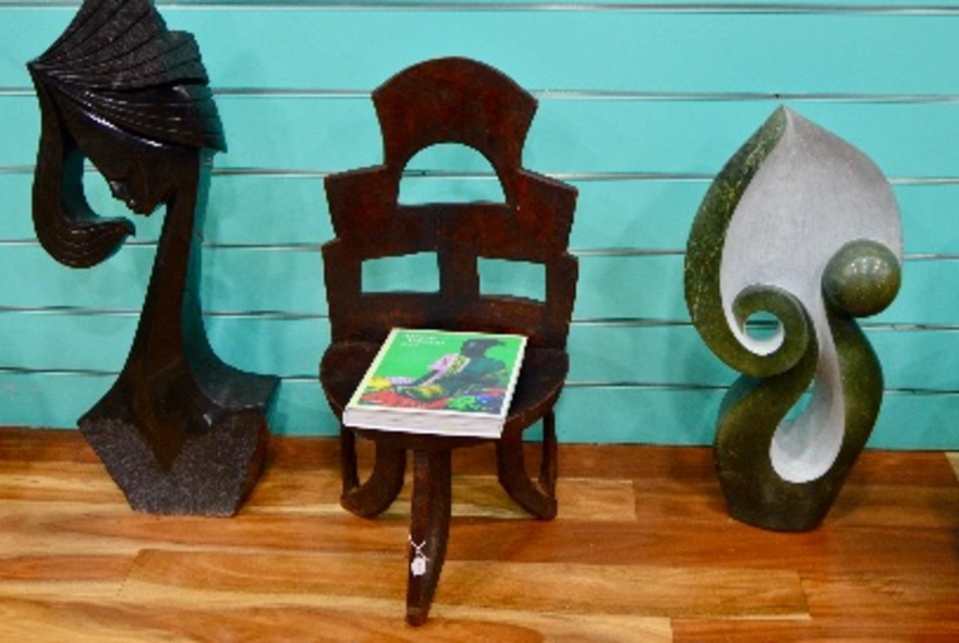 Two sculptures either side of a low wooden chair, against aqua wall.