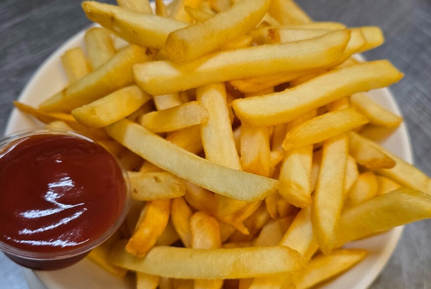 A bowl of chips with a small bowl of tomato sauce on the side. 