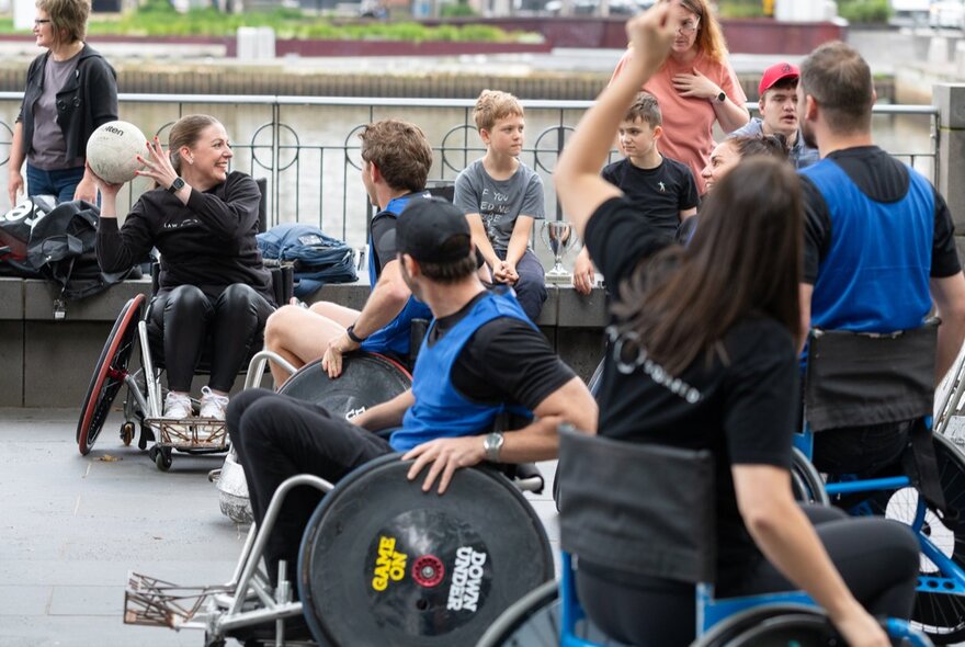 An outdoor area, with several people in wheelchairs engaged in a sporting activity, throwing a ball with their hands and wheeling around the area.