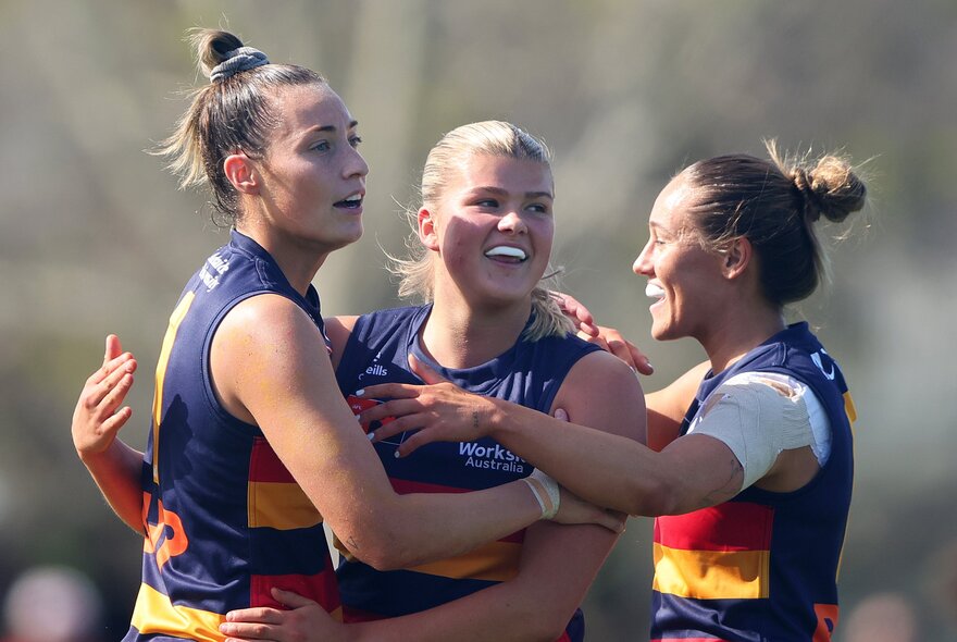 Three Adelaide AFLW players celebrating on the field in a group hug. 