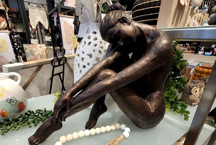 A homewares statue of a seated woman on a shelf.