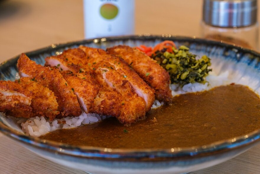 A shallow bowl of curry, alongside it is deep-fried pork slices resting on a bed of white rice.