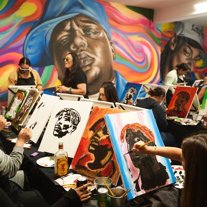 Several rows of people painting on canvases in a room with large, colourful wall murals.