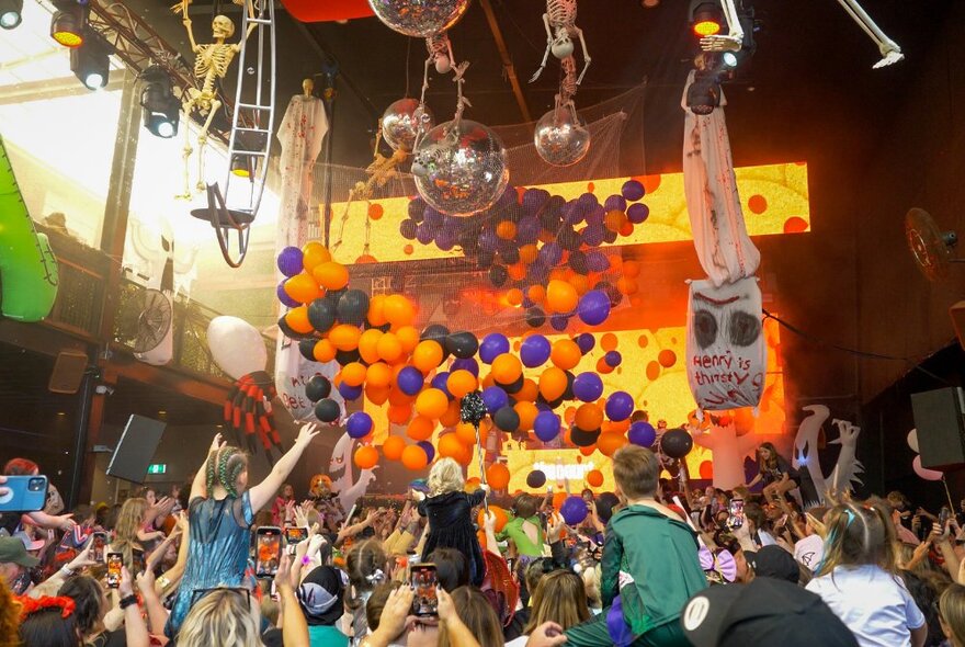 Familes with children in a crowded venue with balloons, mirror balls and decorations.