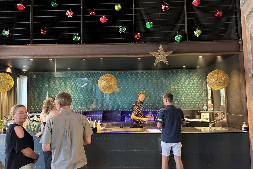 A bar decorated with Christmas baubles and stars with a bartender looking over their shoulder at a customer. 