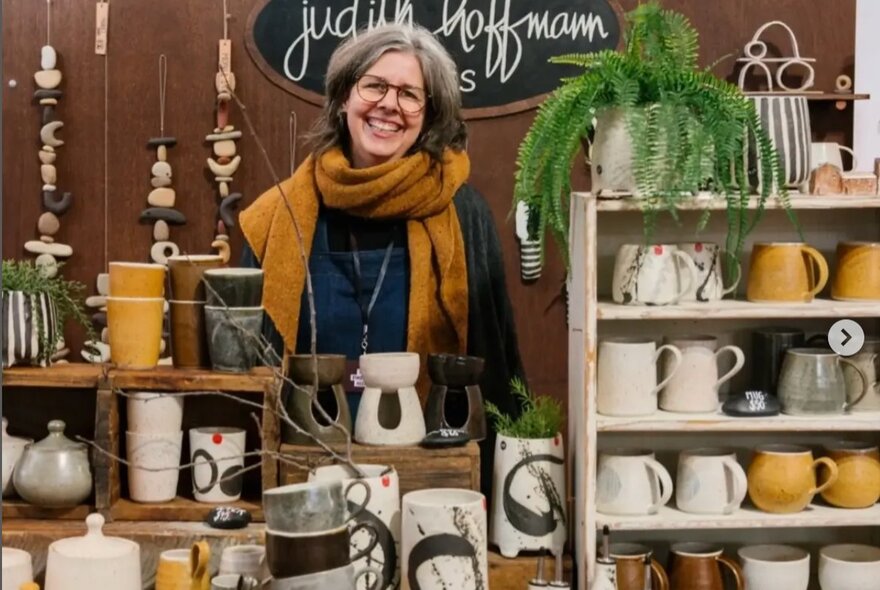 A woman standing behind a market stall of ceramics and other pottery objects.