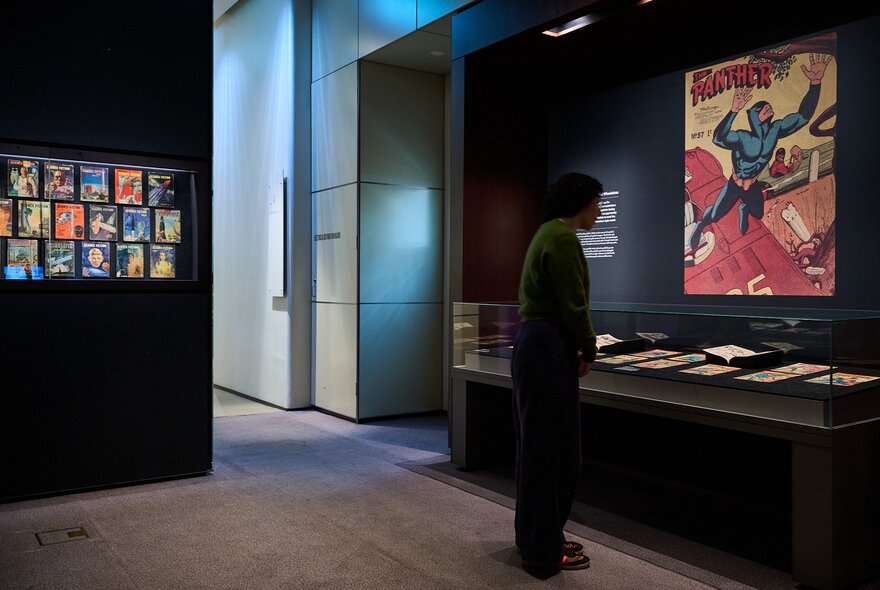 A person at an exhibition in a dark space looking at books in a glass case. 