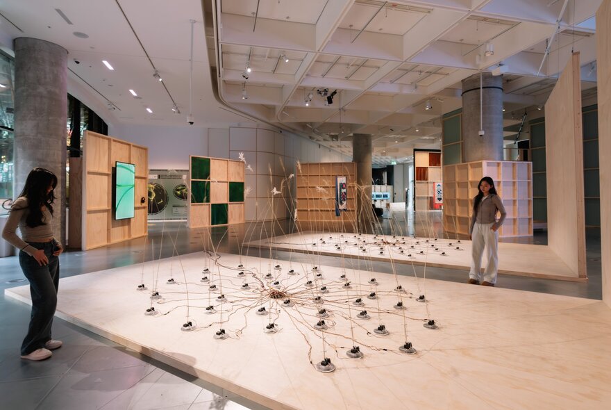 Two young adults observing a spindly floor sculpture in a large gallery space.