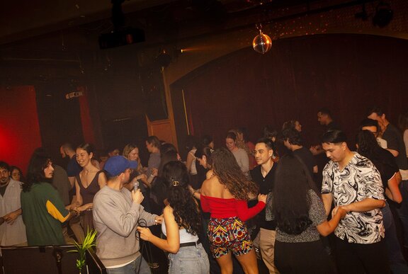 A dimly lit crowded nightclub scene with people dancing on a dance floor.