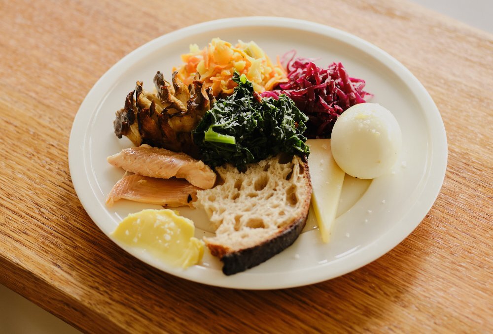 A plate with an egg, bread, salmon, pickles and cheese on it