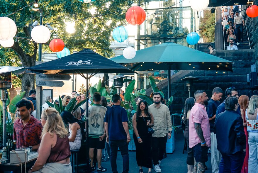 People at an outdoor bar with umbrellas and coloured lights.