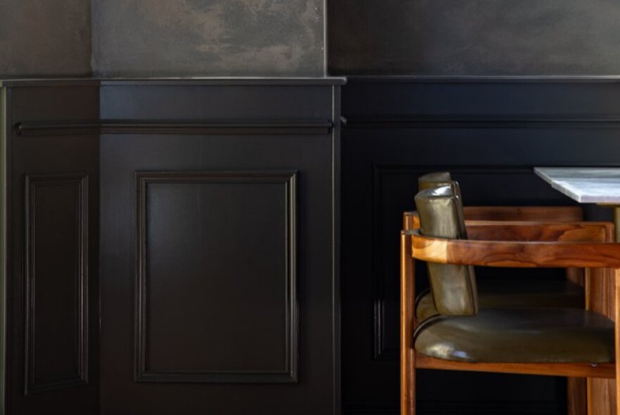 A dark toned wood-panelled restaurant interior with a timber chair and a segment of a table. 