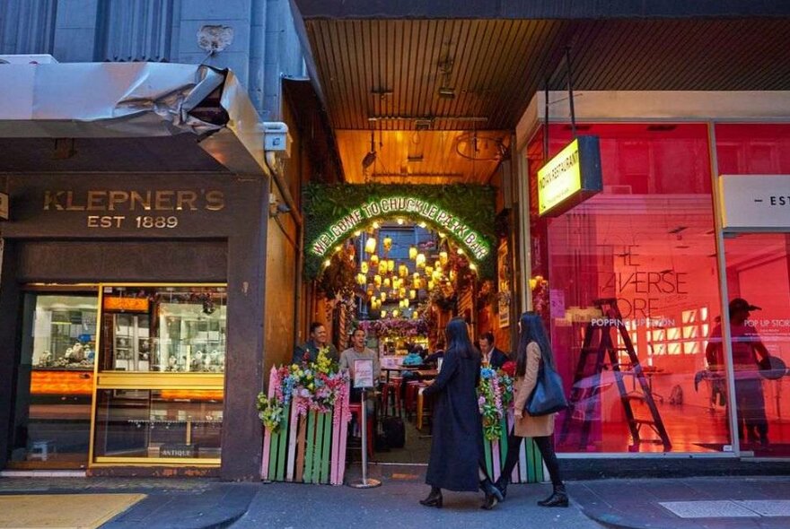 Two women walking into a tiny bar wedged between two retail stores