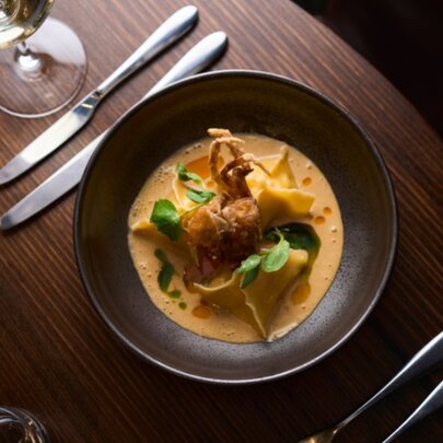 Top down view of a shallow brown bowl with food served in a creamy orange sauce, cutlery alongside.