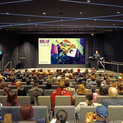 Cinema audience seated in a theatre with rows of seats facing a large screen.