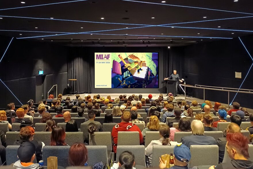 Cinema audience seated in a theatre with rows of seats facing a large screen.