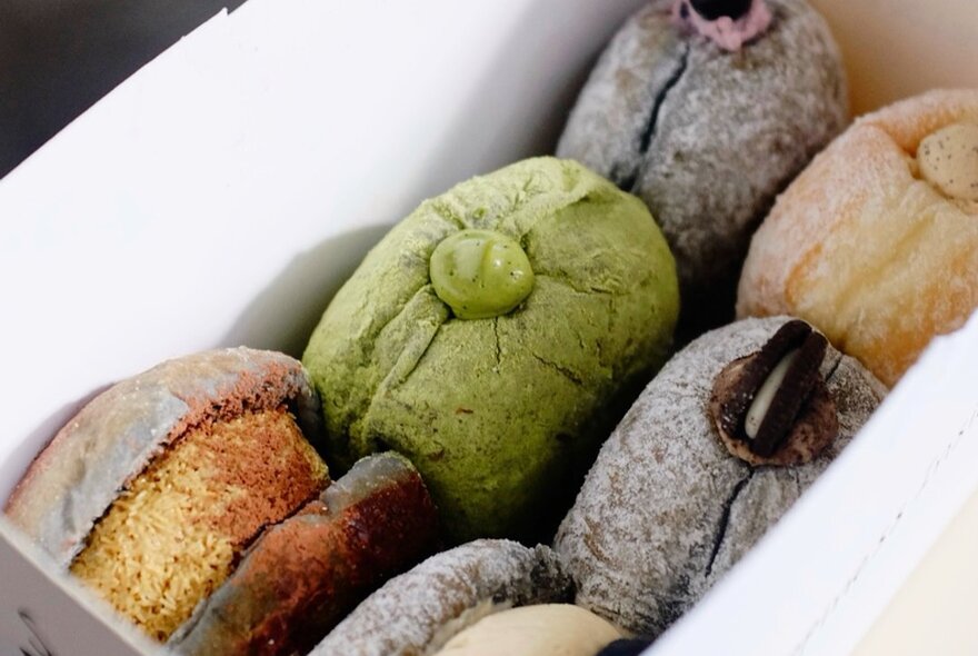 Looking into a box containing six different kinds of filled donuts.
