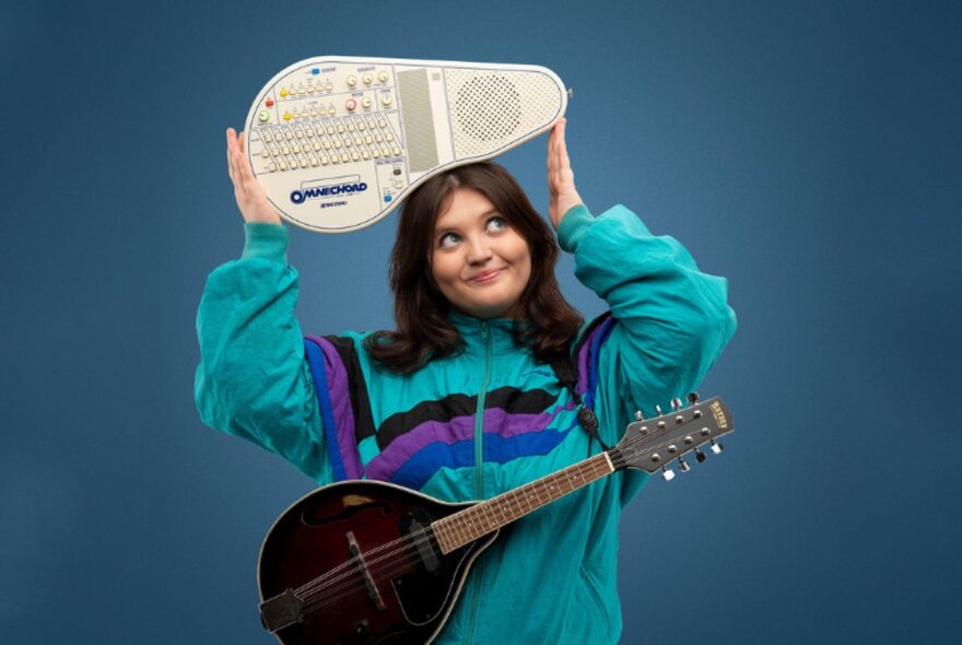 Comedian Sez holding an omnichord above her head with a mandolin over her shoulders.