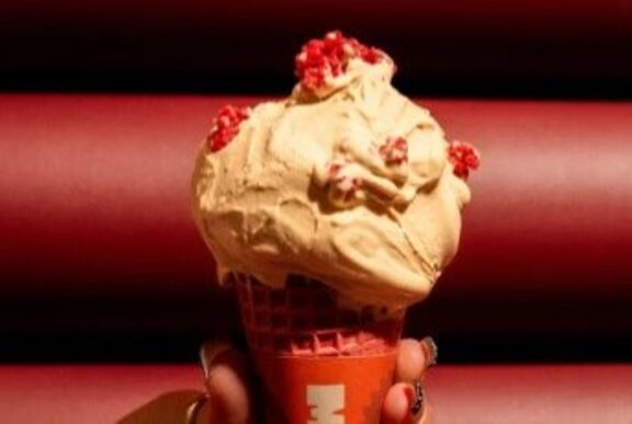 A scoop of coffee ice cream on a red cone in a red cardboard sleeve.