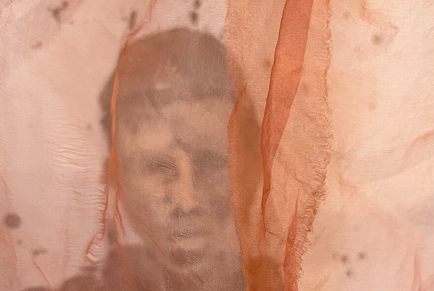A pale orange coloured piece of chiffon fabric with an image of a face behind it.