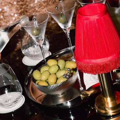 A waiter's tray with a bowl of olives, a red mini-lamp with three martini glasses and two water glasses, with a waiter pouring water.