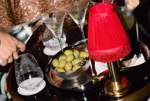 A waiter's tray with a bowl of olives, a red mini-lamp with three martini glasses and two water glasses, with a waiter pouring water.