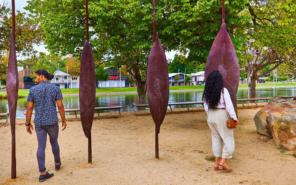 A couple walking through an art installation with large shield sculptures by the river.