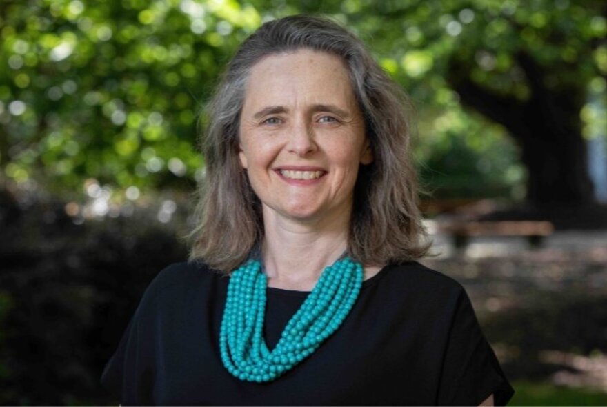 Portrait of Dr Jen Martin, smiling, in front of a large tree blurred in the background.