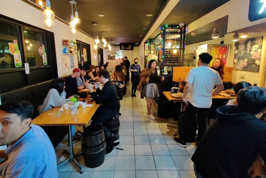 People seated at dining tables inside a casual restaurant eating and drinking.