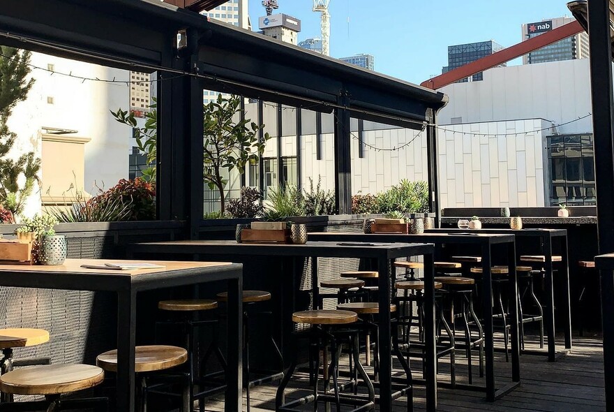 Empty rooftop bar of Goldilocks during the day with tables and stools showing cityscape in background.