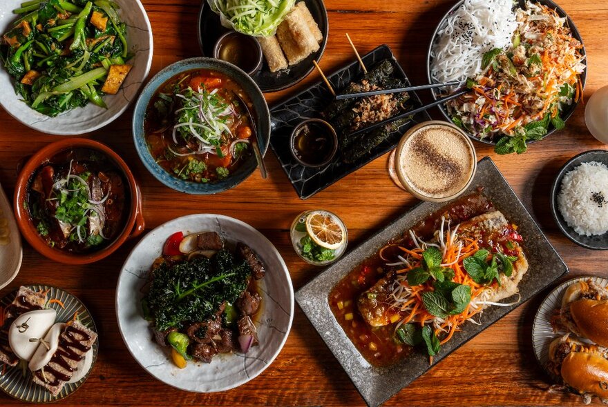 Looking down on assortment of Vietnamese dishes and condiments on a wooden table.