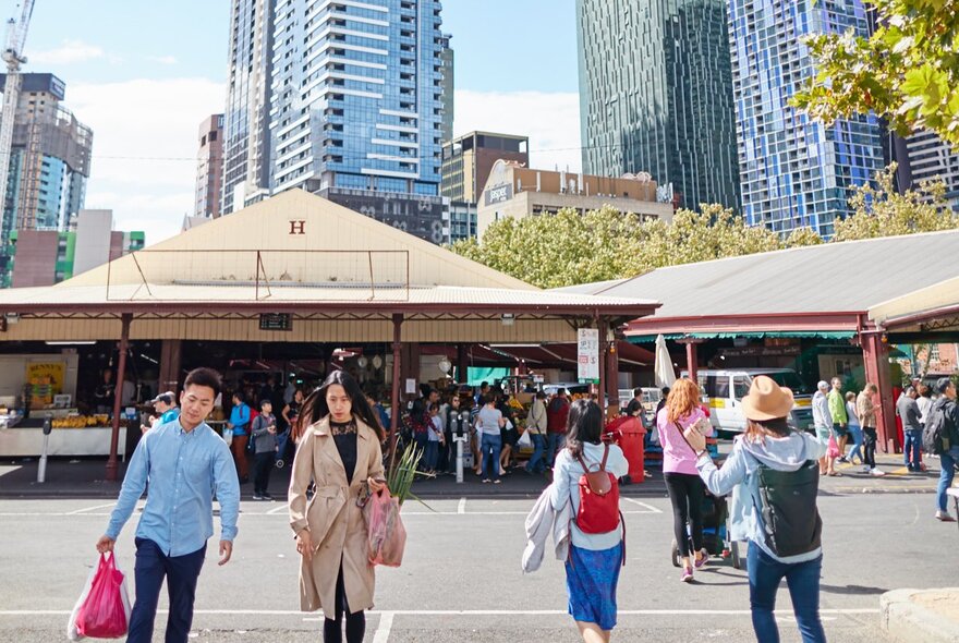 View of the sheds at Queen Victoria Market, with people walking around and city buildings in the background.