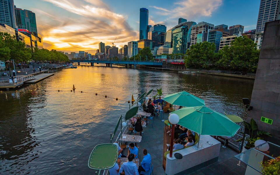Sun setting down over the Yarra River with people sitting at a bar.
